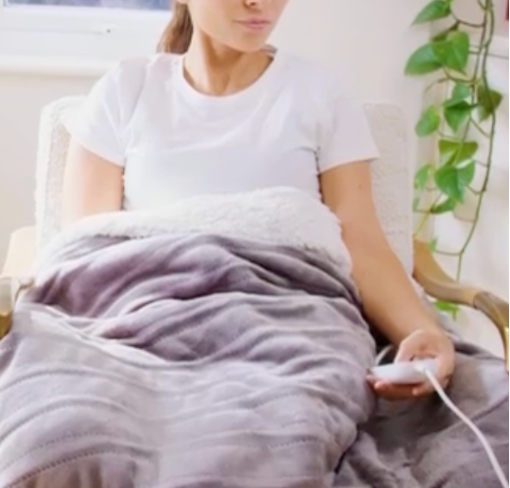Femme frileuse qui s'installe dans son fauteuil et allume son plaid chauffant avec la télécommande- les meilleurs plaids de l'hiver 2026 pour frileuses.